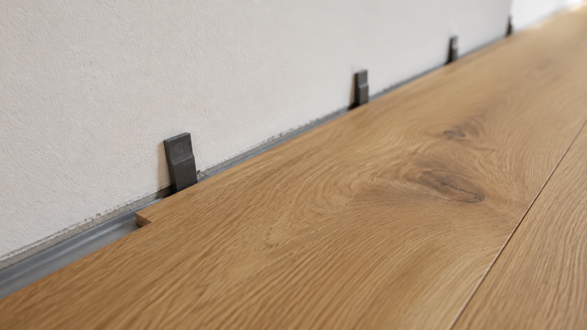 Nahaufnahme an der Wand: Distanzkeile zwischen erster Plankenreihe und Putz, darunter die Dämmunterlage.